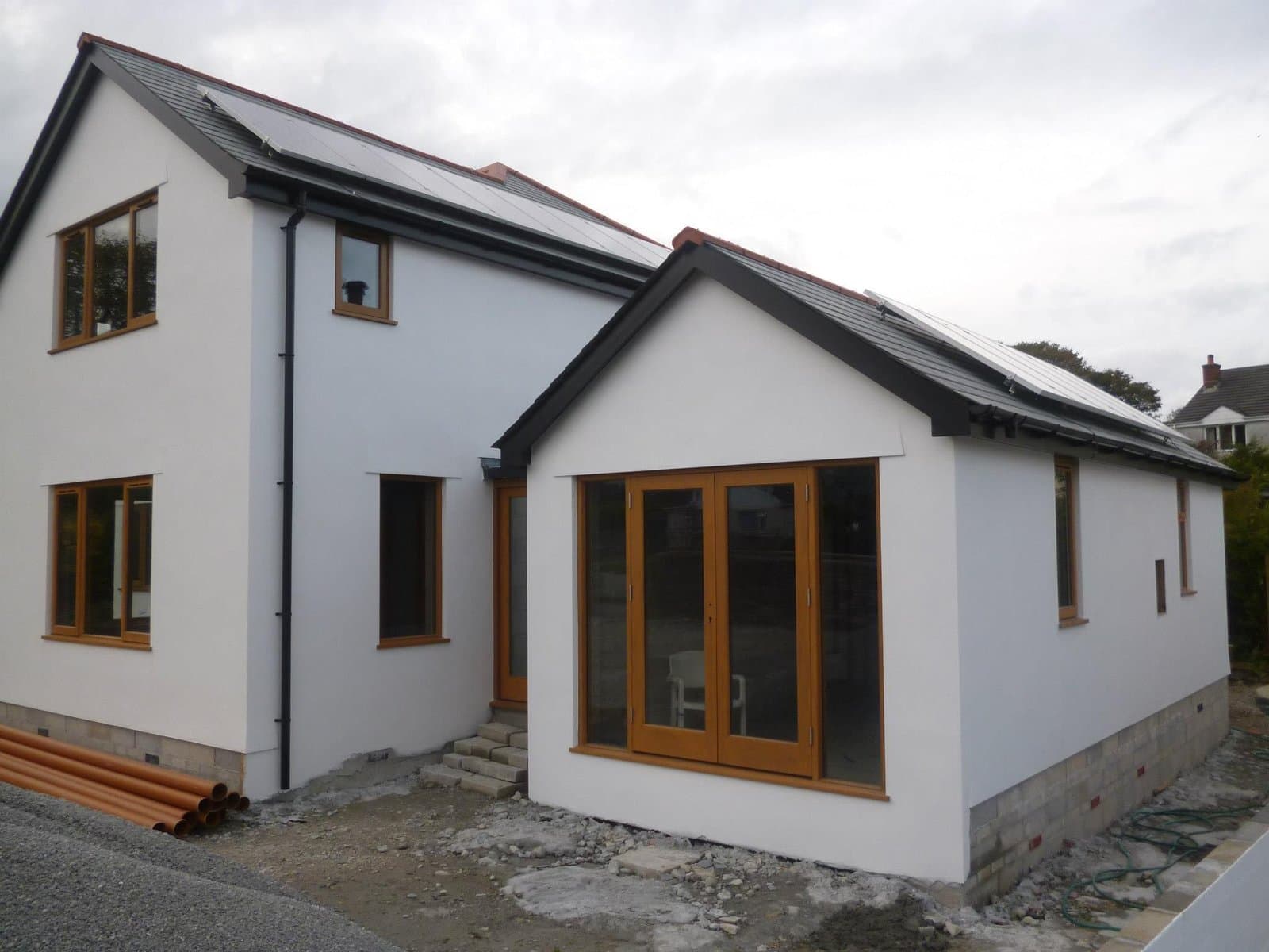 White-rendered new-build home with bespoke timber bi-fold doors, casement windows and matching frames throughout — PAS24-compliant joinery by K.Davey.