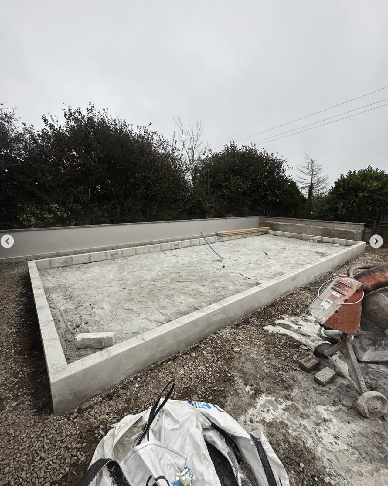 Fresh concrete foundation slab with perimeter wall ready for the annex build — original site state