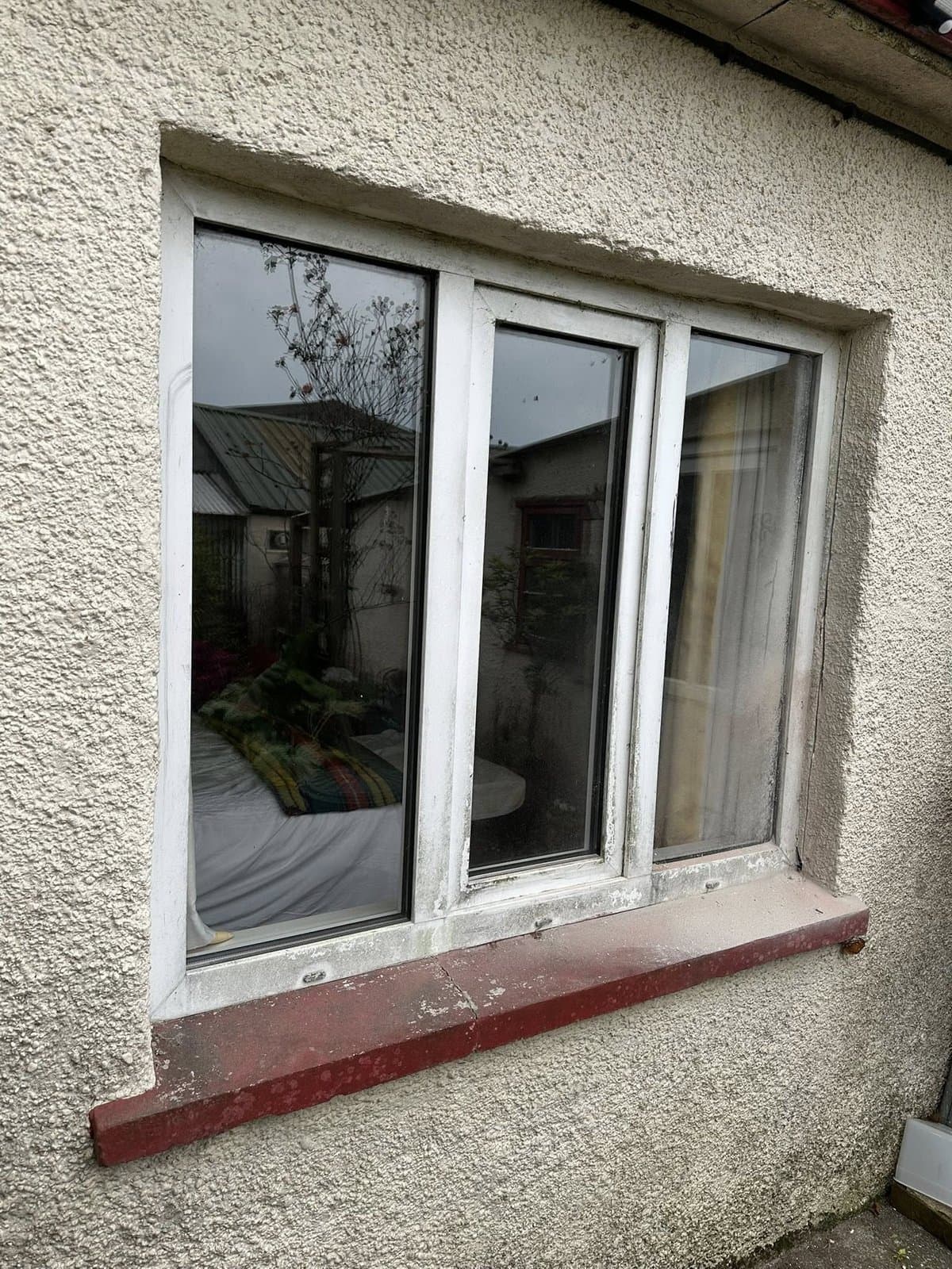 Aged PVC three-pane window with stained sill on a Devon village cottage — original state before restoration