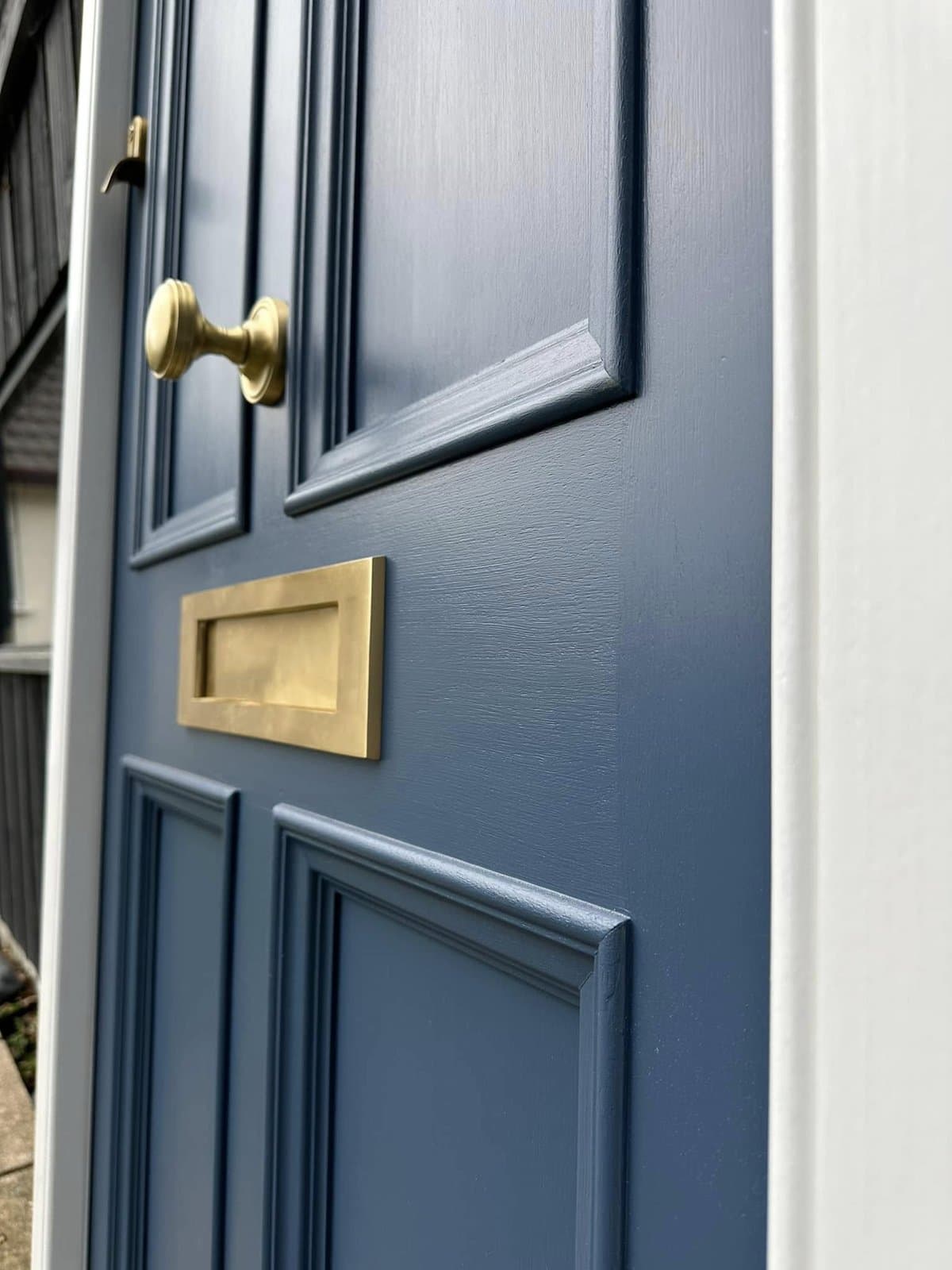 Close-up of a slate-blue painted timber front door with brass knob and brass letterplate