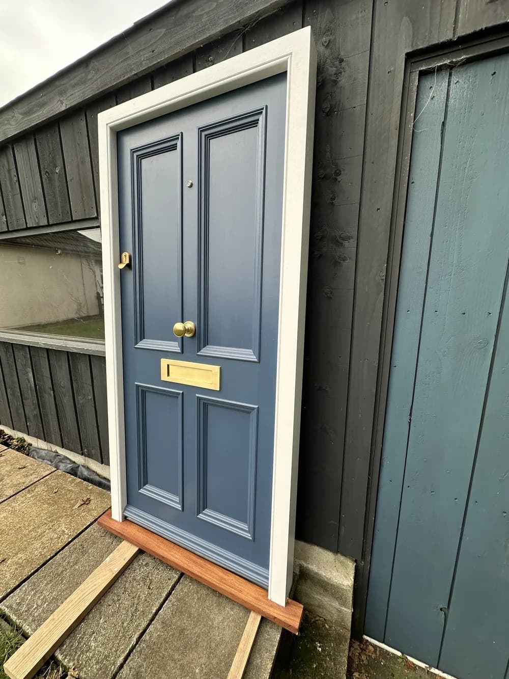 Slate-blue bespoke timber front door with brass hardware on a coastal cottage