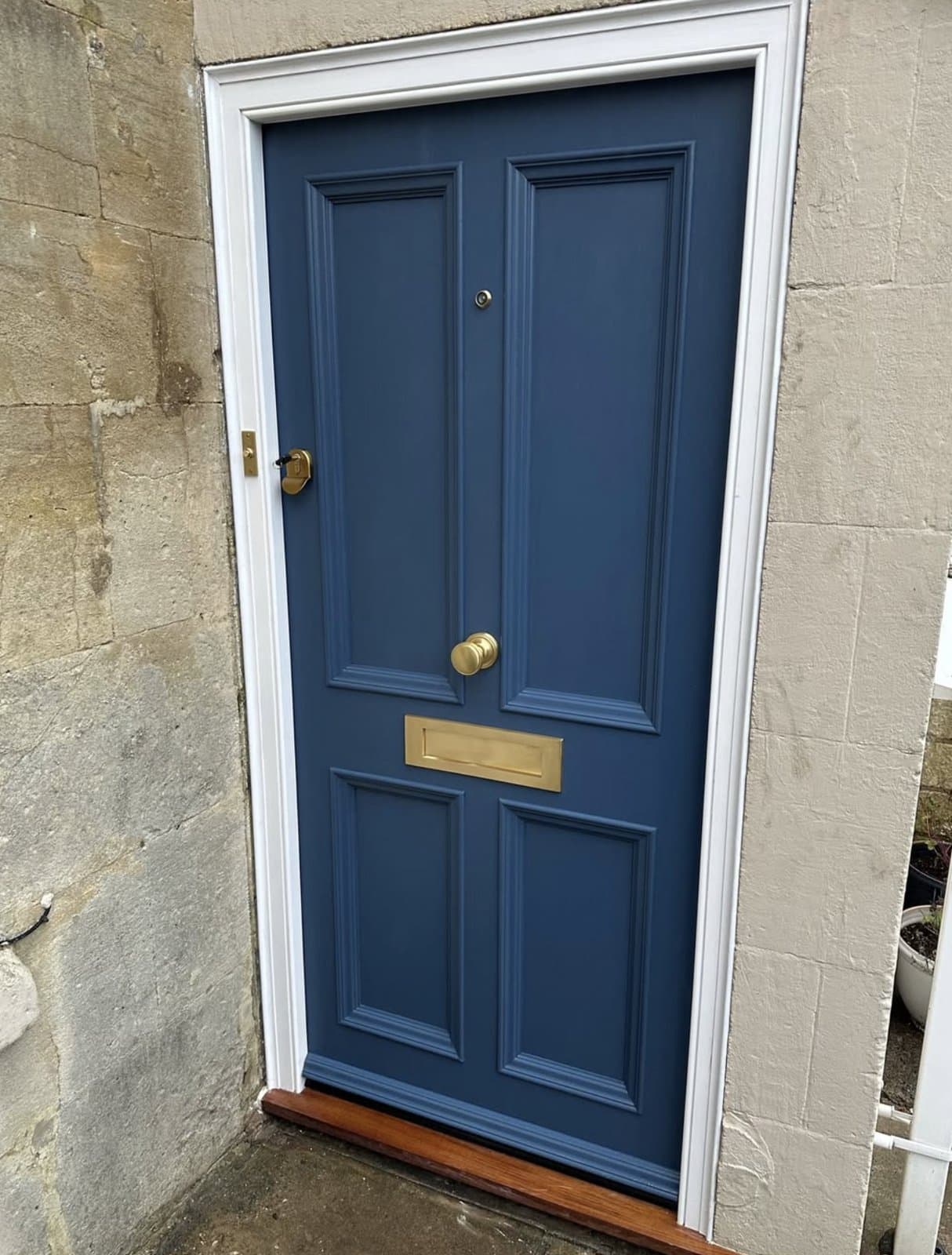 Bespoke slate-blue painted timber front door fitted into a stone-walled property — brass knob, brass letterplate and crisp white frame, finished installation by K.Davey.